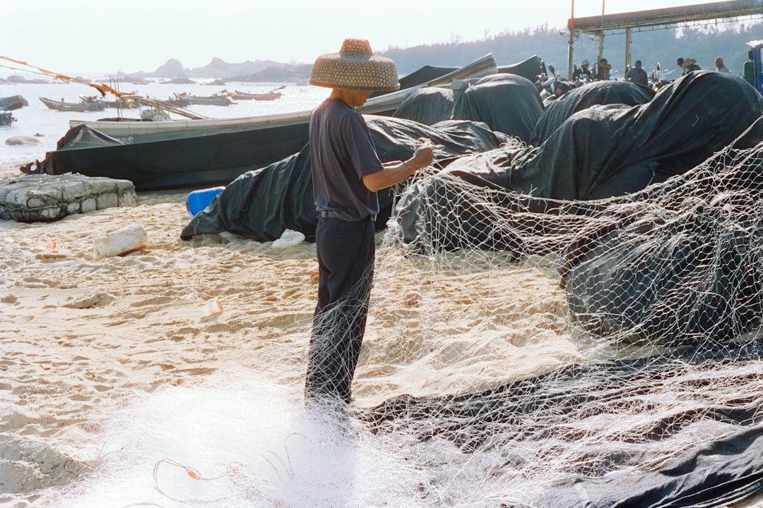 A fisherman mending a fishing net on a sandy beach, reflecting daily life in Gwadar's fishing settlements