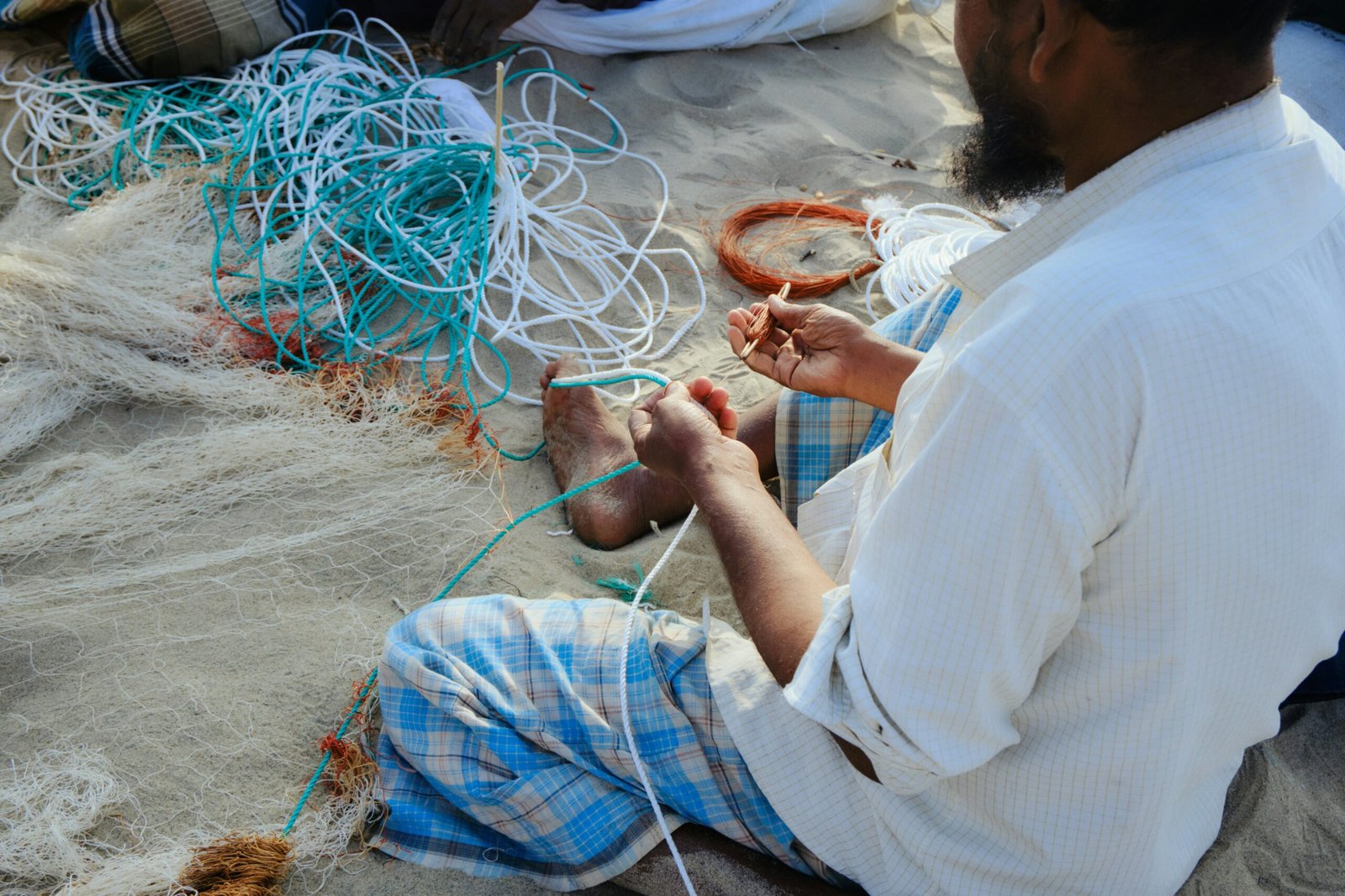 Fisherman repairing a fishing net on sandy ground, representative image for Balochistan's coastal fishing communities including Gwadar