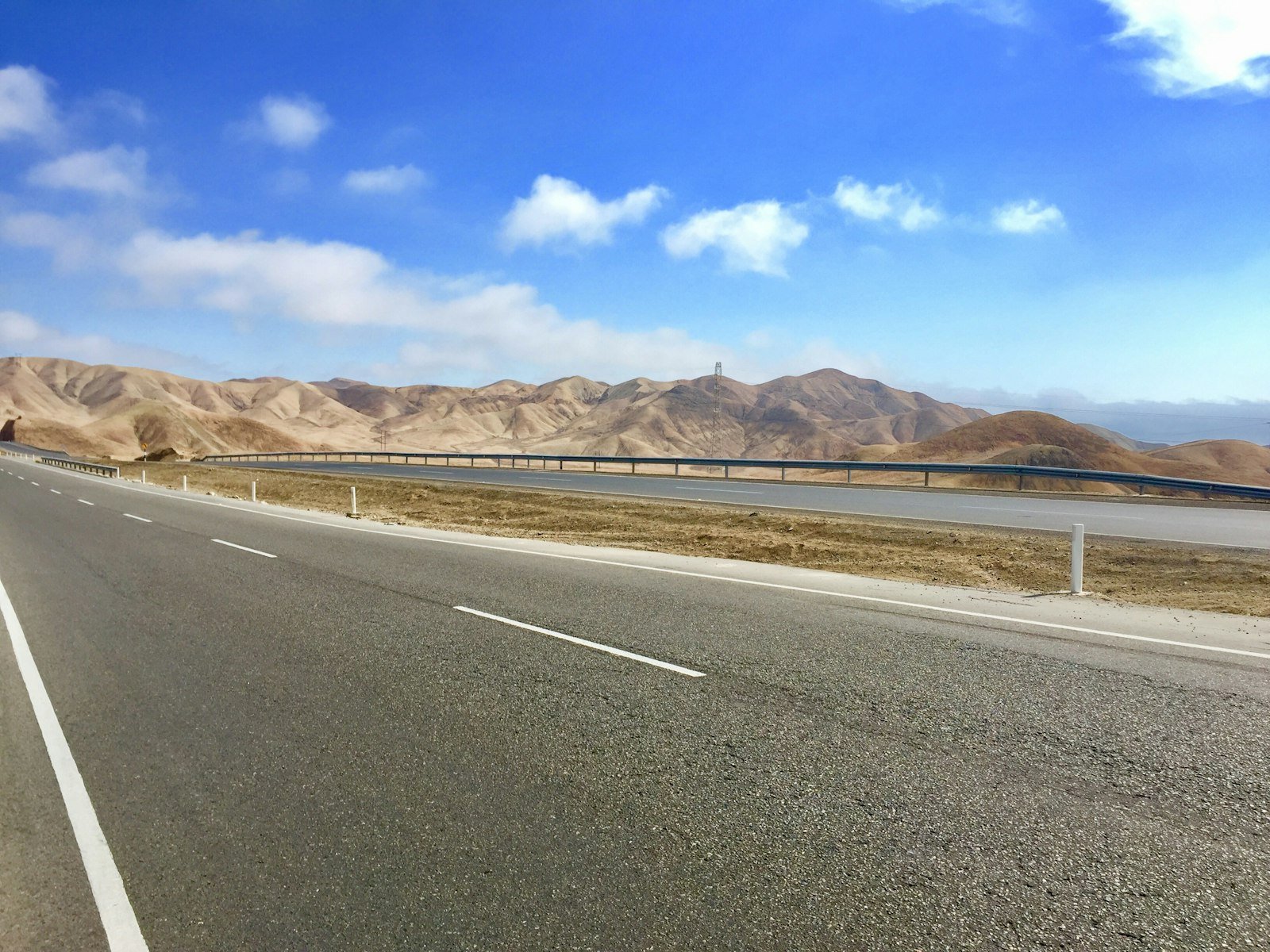 Paved road cutting through brown mountainous terrain under a clear sky, representative of the Makran coastal highway linking Karachi, Lasbela, Hub, and Gwadar