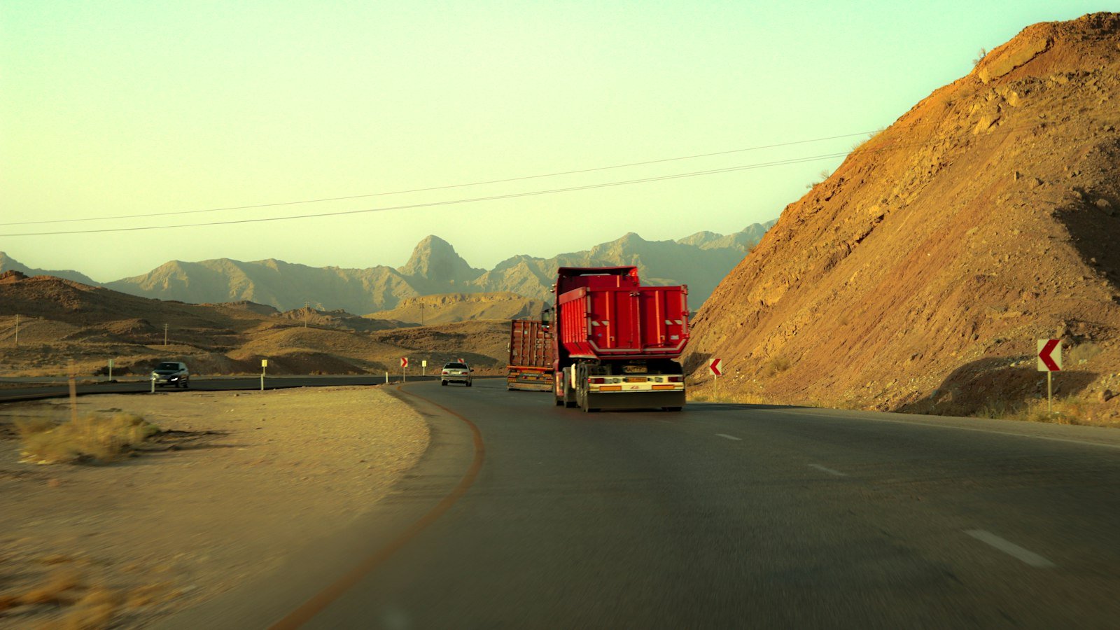 A truck travelling a desert road flanked by mountains, representative of the overland trade and transport routes crossing Balochistan's Makran coast